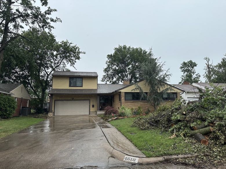 Storm-damaged yard with a large downed tree and debris piled beside a house