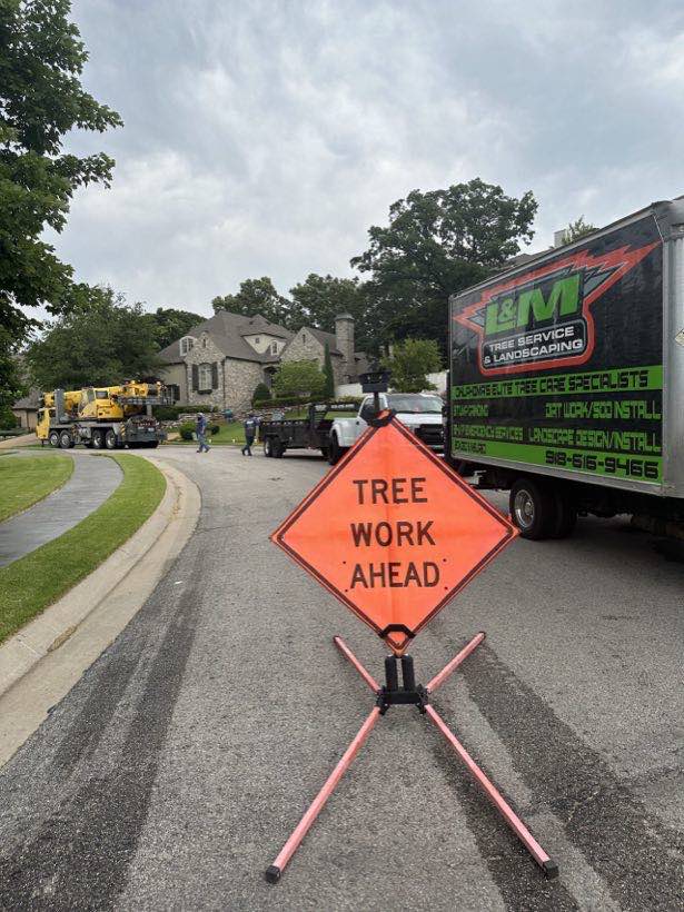 L & M Tree Service box truck and crane on a residential street with a Tree Work Ahead sign